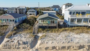 Una propiedad frente a la playa con varias casas, incluyendo una casa destacada con balcón y una escalera que conduce a una terraza.