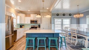 Una cocina moderna con armarios blancos, una isla grande con taburetes de bar, electrodomésticos de acero inoxidable y un comedor con mesa y sillas.