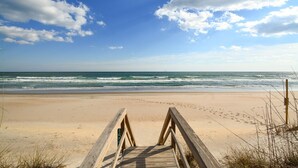Un paseo marítimo de madera que lleva a una playa arenosa, con el océano al fondo.