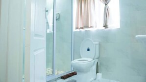 Un baño con cabina de ducha de vidrio, inodoro y ventana con cortinas.