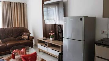 A modern living room with a brown leather sofa, a glass coffee table, and a red chair. There is a built-in TV and a refrigerator.