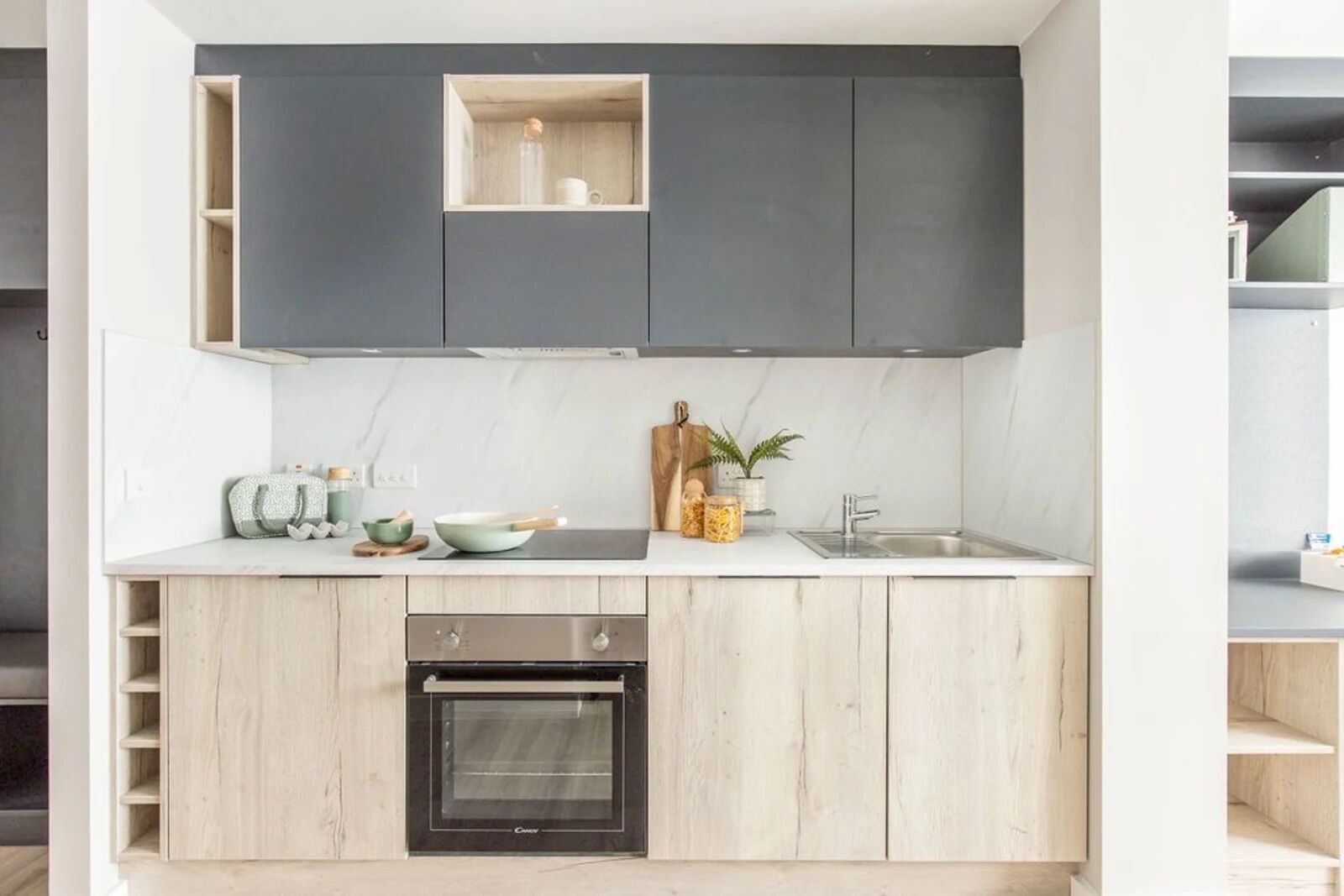 A modern kitchen with grey cabinets, a built-in oven, a sink, and a countertop with various kitchen items.
