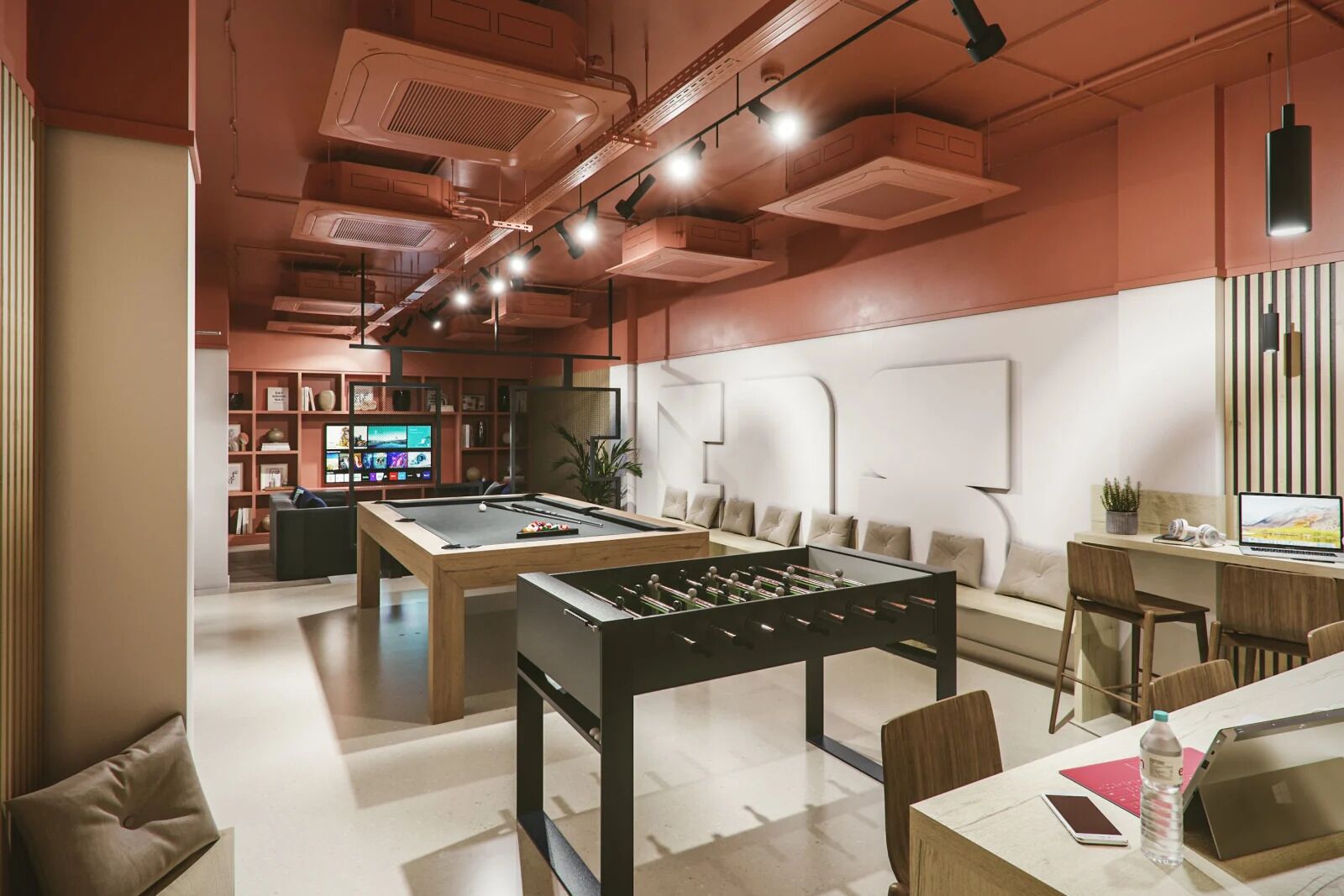 Un espace de détente moderne comprenant une table de baby-foot, une table de billard et un coin salon confortable avec des canapés et une table basse.
