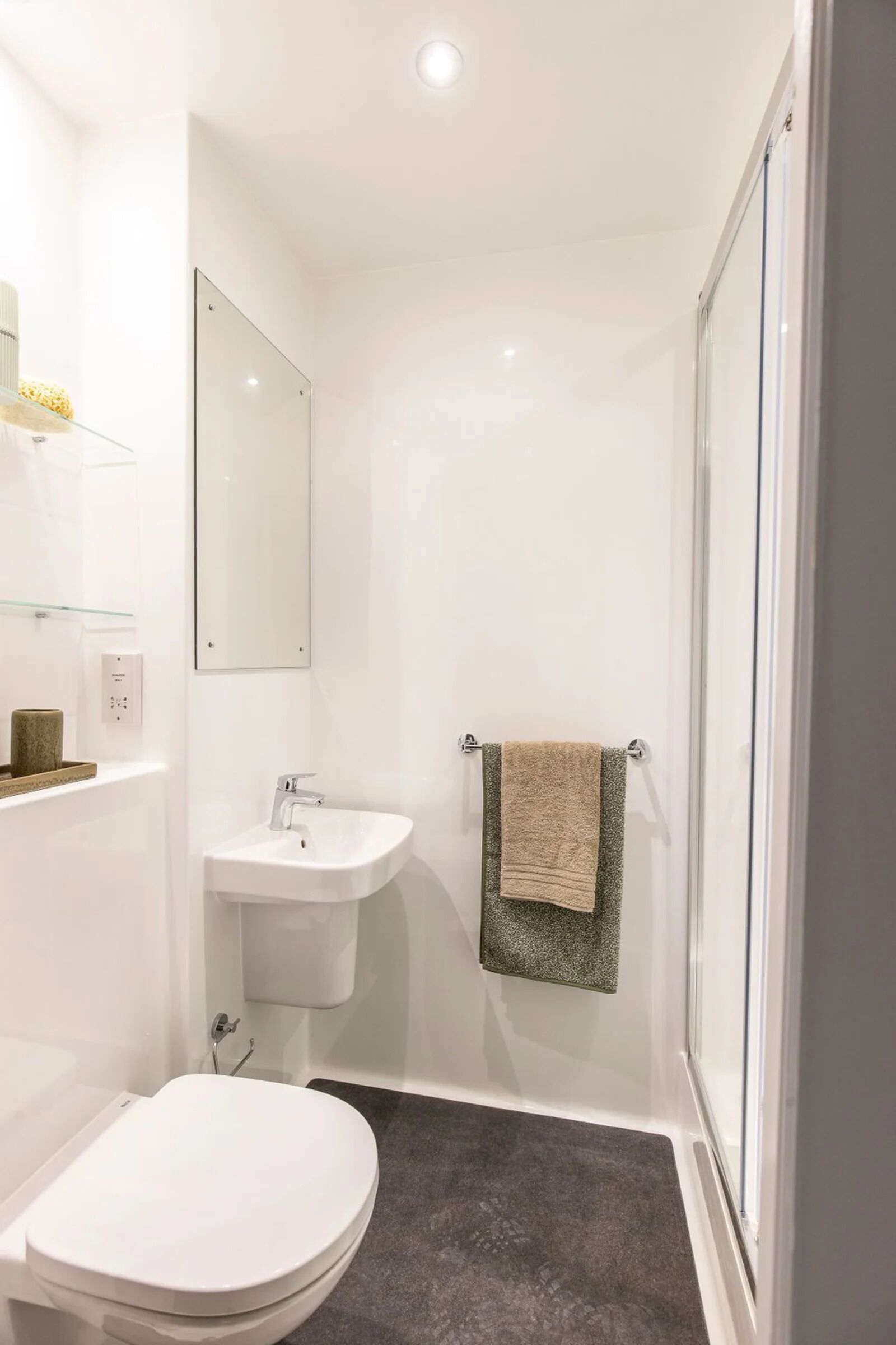 Et moderne badeværelse med toilet, vask og glasvæg ved brusebad.