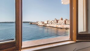 A view from a window overlooking a waterfront with buildings and a clear sky. - Una Finestra Su Cala Rossa by Wonderful Italy (Syracuse)