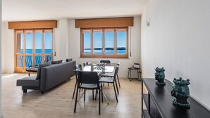 A modern living room with a sofa, dining table, and chairs, large windows with a view of the sea, and decorative vases on a side table. - Una Finestra Su Cala Rossa by Wonderful Italy (Syracuse)