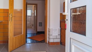 Una puerta de madera abierta que da a un pasillo con suelo de baldosas, un felpudo y una pared blanca con un termostato.