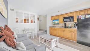 A modern living room with a grey sofa, a small coffee table, and a dining area with white chairs. - Oceanfront Condo Balcony with Resort Pool Hot Tub (North Myrtle Beach)