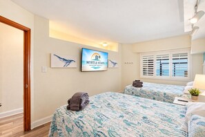 A hotel room with two beds, a television displaying 'MYRTLE STAYS Vacation Rentals', and a window with blinds.