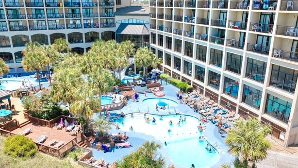 A hotel with multiple swimming pools, palm trees, and outdoor seating areas. - Oceanfront Condo Balcony with Resort Pool Hot Tub (North Myrtle Beach)