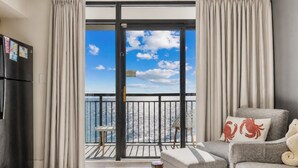 A modern living room with a balcony, a sofa, a small table, and a white chair. - Oceanfront Condo Balcony with Resort Pool Hot Tub (North Myrtle Beach)