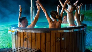 Una bañera de hidromasaje de madera con personas adentro, rodeada por un área verde.