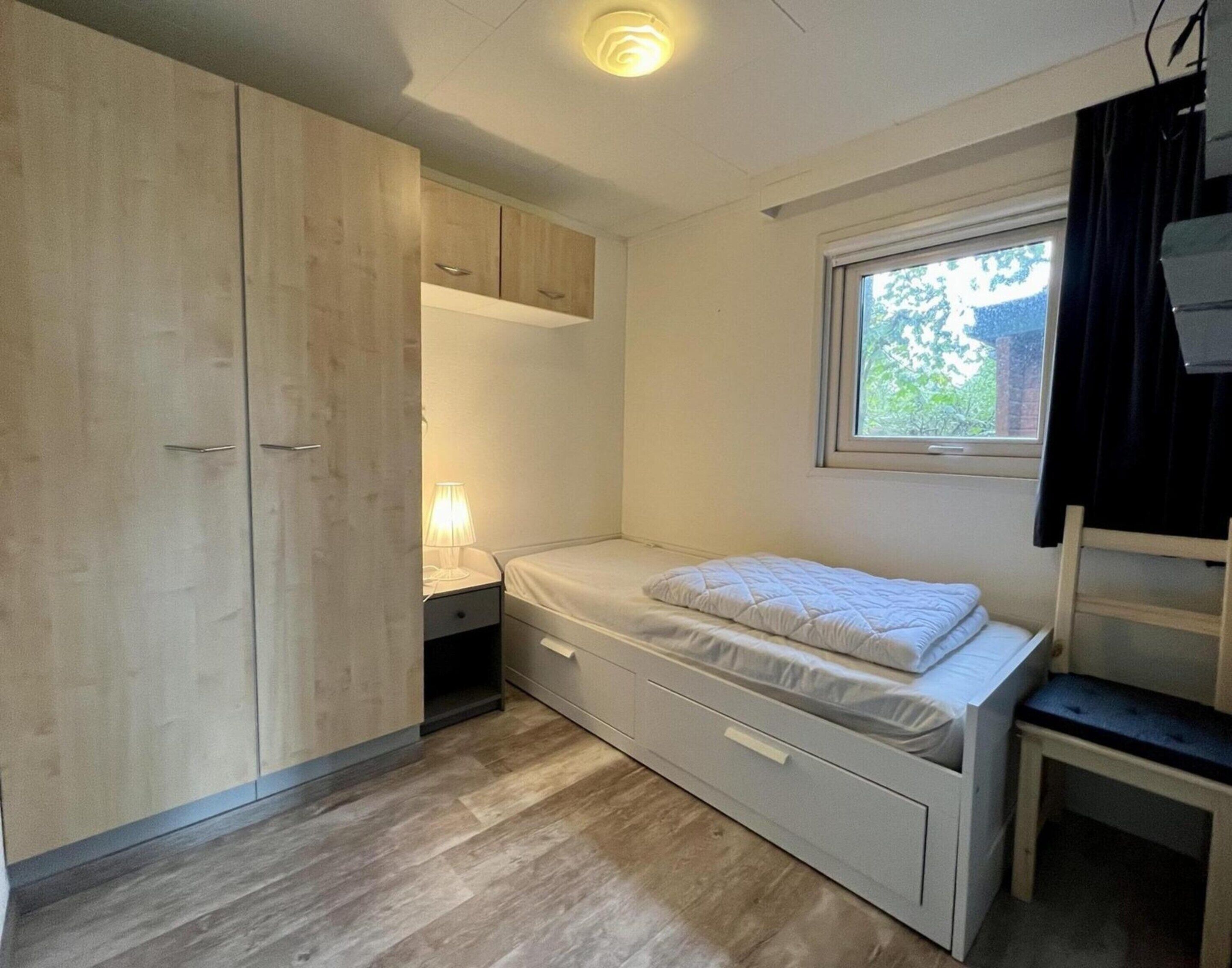 A compact bedroom with a bed, a wardrobe, a desk, and a window.
