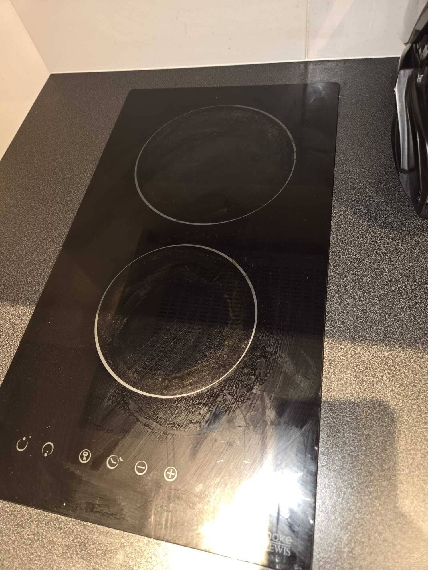 Une plaque de cuisson à induction noire, dotée de deux zones de cuisson circulaires et d’un panneau de commande avec différents boutons.