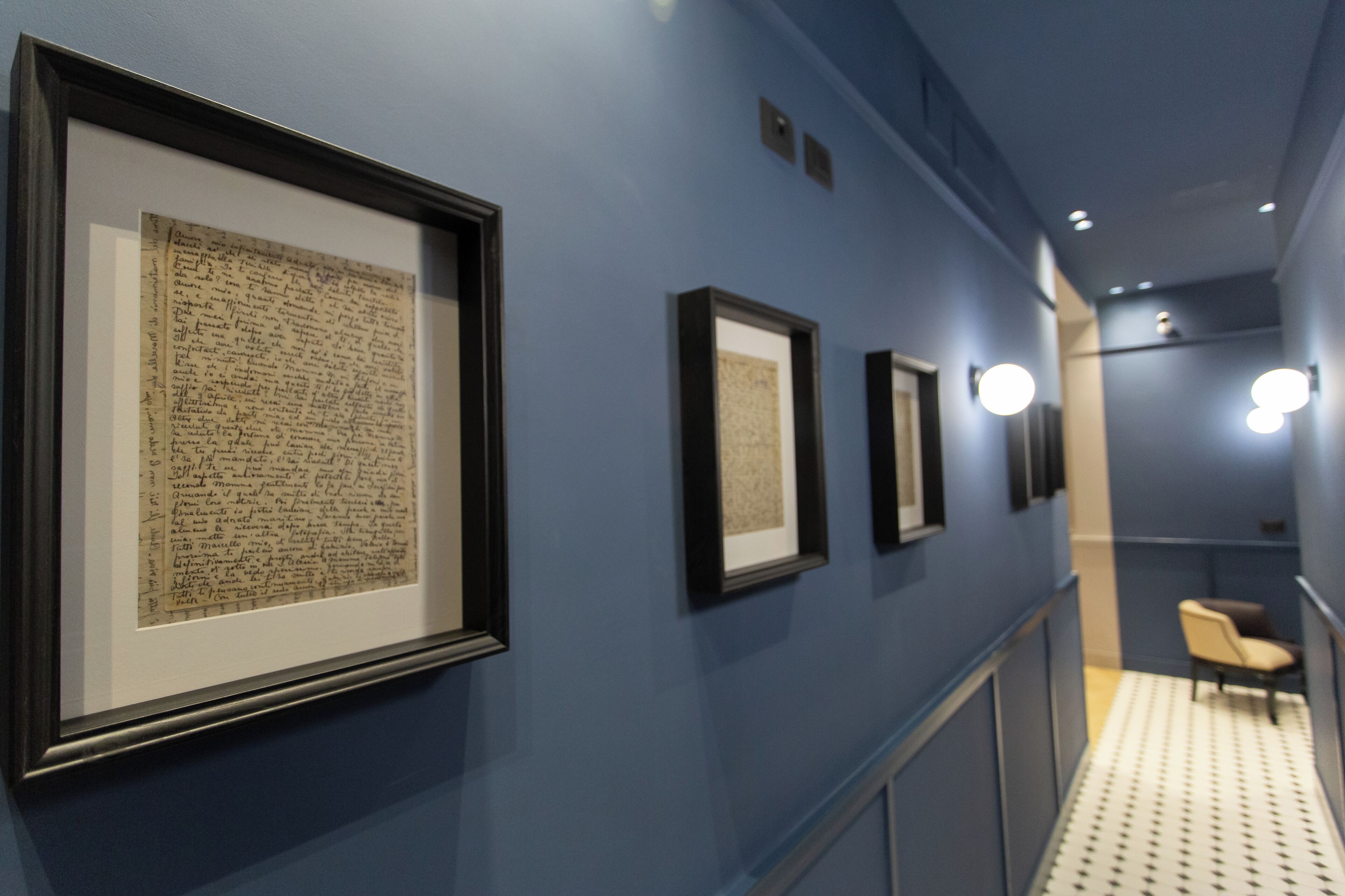 A hallway with framed documents on the wall, a chair, and a patterned floor.