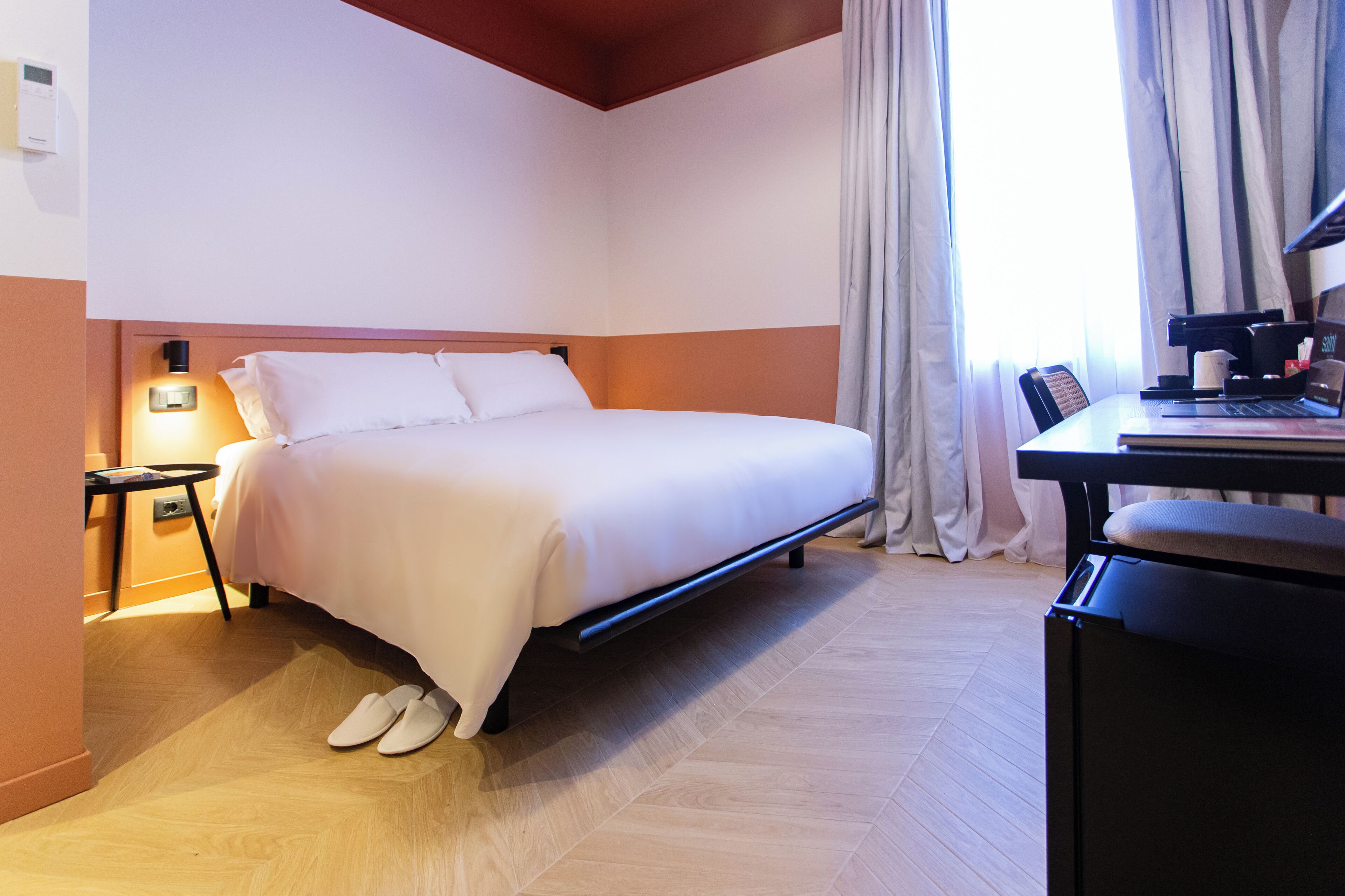 Quarto de hotel com uma cama, uma mesa de escritório com um laptop e uma máquina de café.