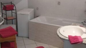 A bathroom with a bathtub, a sink, and a chair with red towels. - 3-ROOM APARTMENT NEAR TOWN CENTER (Obernai)