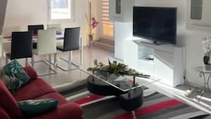 A modern living room with a red sofa, a glass coffee table, and a flat-screen TV on a white cabinet. - 3-ROOM APARTMENT NEAR TOWN CENTER (Obernai)