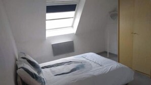 A small, simple room with a bed, a skylight, and a door. - 3-ROOM APARTMENT NEAR TOWN CENTER (Obernai)
