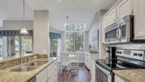 Una cocina moderna con encimeras de granito, electrodomésticos de acero inoxidable y una zona de comedor con sillas blancas.