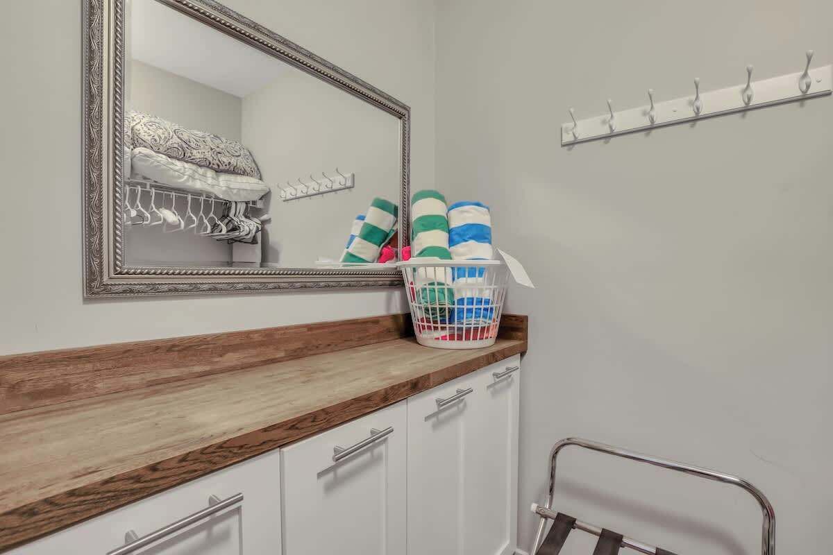 Een badkamer met een houten wastafelmeubel, een spiegel, een handdoekrek en een mand met opgevouwen handdoeken.