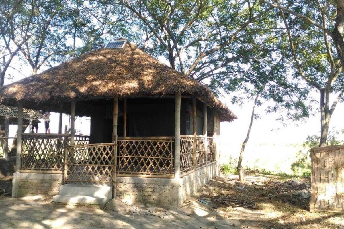 A thatched-roof hut with a lattice railing, surrounded by trees.