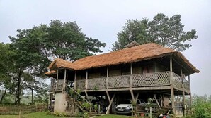 Ein zweistöckiges Holzhaus mit Strohdach, umgeben von Bäumen und einem eingezäunten Garten.