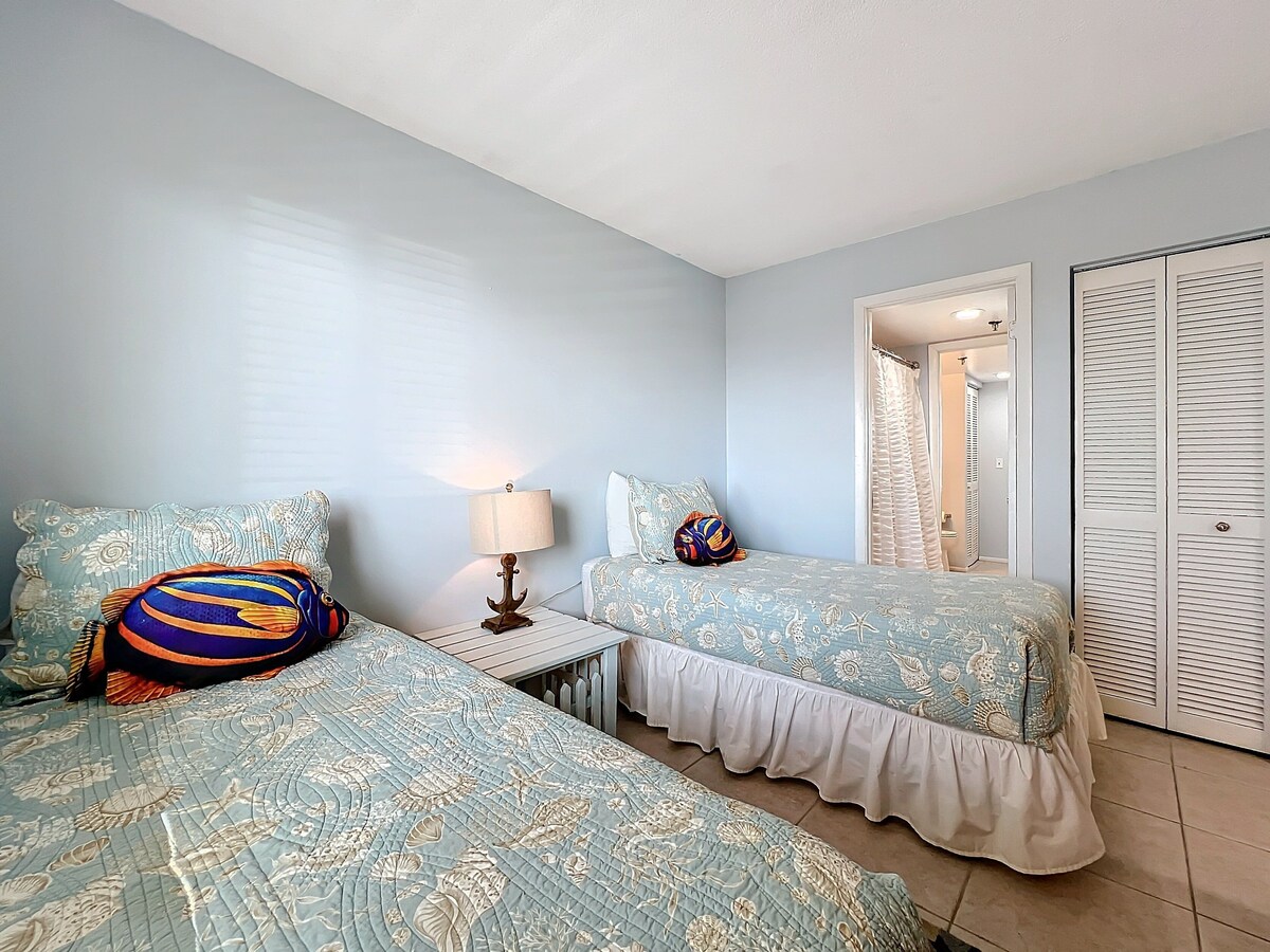 This delightful twin bedroom boasts coastal bedding, vibrant decor, and private en-suite access, offering a comfortable and convenient stay for guests.