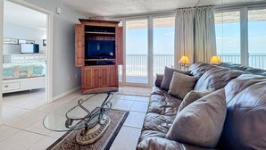 A living room with a sofa, a television on a wooden cabinet, and a balcony with curtains.