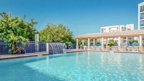Une piscine aux eaux cristallines agrémentée d’une cascade, entourée de chaises longues et d’un espace salon abrité.