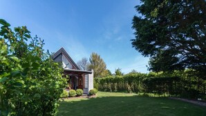 A house with a sloped roof, a front porch, and a well-maintained lawn. - Bungalow in North Holland Coast (Sint Maartensvlotbrug)