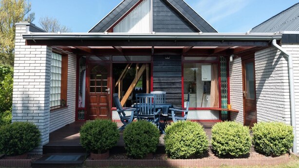 A house with a gabled roof, a front porch with a table and chairs, and a brick exterior. - Bungalow in North Holland Coast (Sint Maartensvlotbrug)