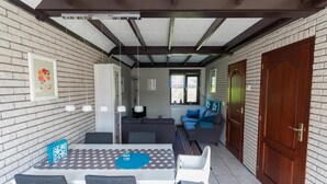 A dining area with a table and chairs, a sofa, and a window with blinds. - Bungalow in North Holland Coast (Sint Maartensvlotbrug)