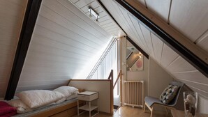 A compact attic bedroom with a sloped ceiling, a bed, a small desk, a chair, and a radiator. - Bungalow in North Holland Coast (Sint Maartensvlotbrug)