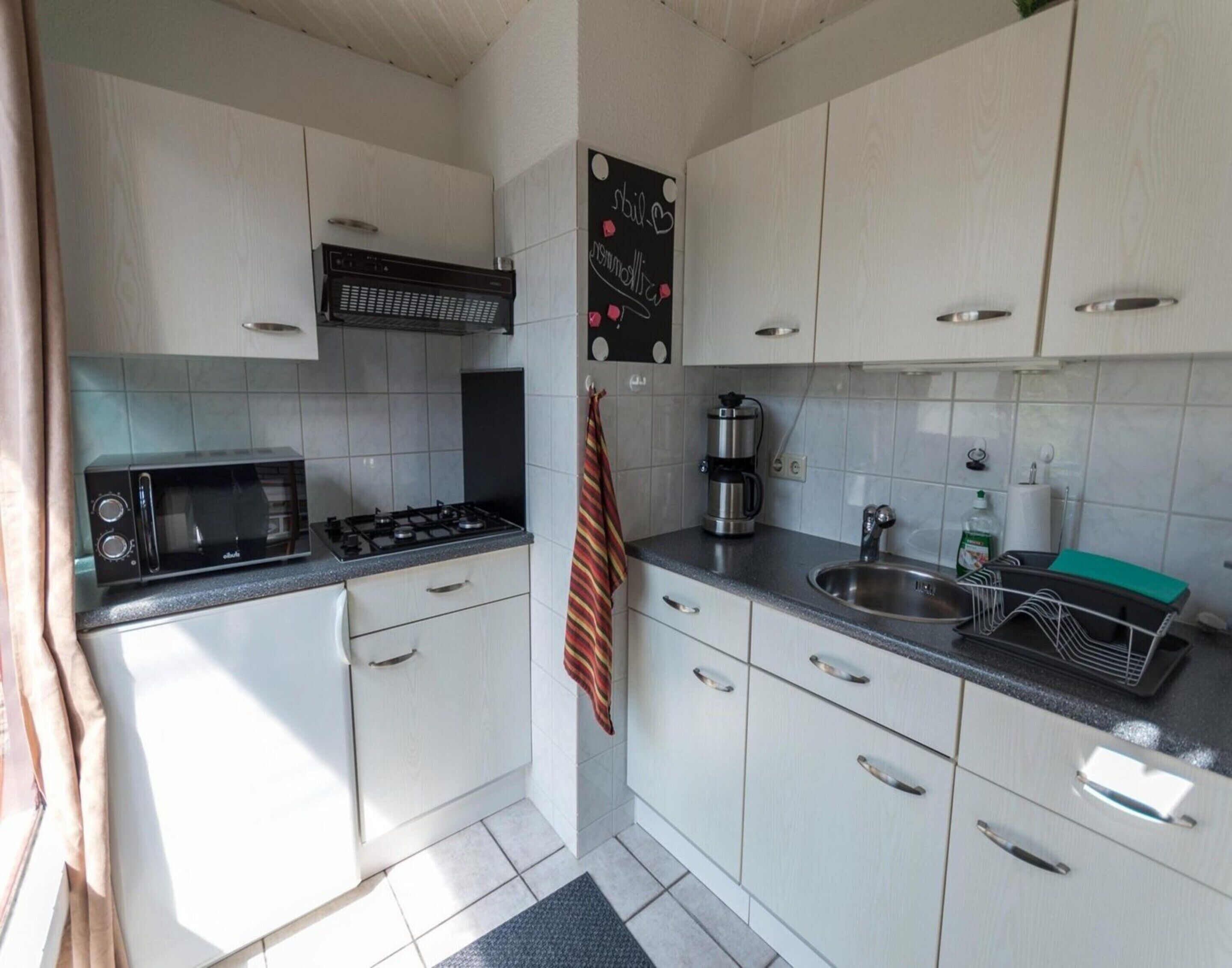 A compact kitchen with white cabinets, a microwave, a stove, a coffee maker, and a sink.