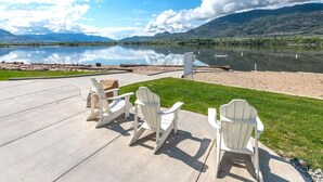 A lakeside patio with Adirondack chairs, a concrete deck, and a view of a lake and mountains. - Sky-View Cottage - 5 Bedroom View home 265 (Osoyoos)