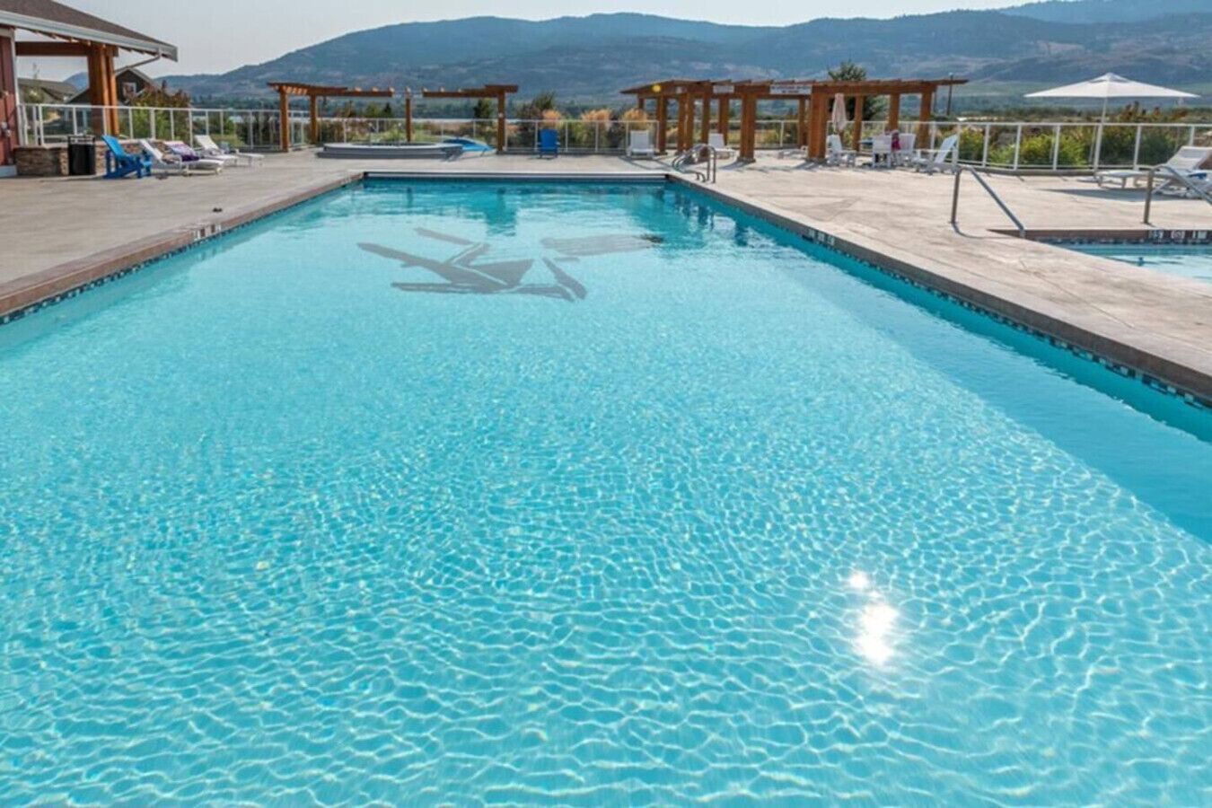 Una piscina rectangular con agua cristalina, rodeada de sillones de descanso y una pérgola de madera.