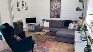A modern living room with a grey sectional sofa, a teal armchair, a flat-screen TV, a small side table, and a colorful rug. - Bungalow Near Beach With Garden (Sint Maartensvlotbrug)
