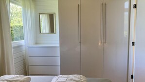 A bedroom with a bed, a wardrobe, and a window with curtains. - Bungalow Near Beach With Garden (Sint Maartensvlotbrug)