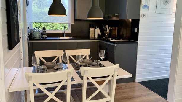 A compact kitchen with a dining table set for four, featuring white chairs with a crisscross back design. - Bungalow Near Beach With Garden (Sint Maartensvlotbrug)