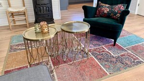 A cozy living room with a dark green armchair, a wooden chair, a black stove, and two small round tables with metal legs. - Bungalow Near Beach With Garden (Sint Maartensvlotbrug)