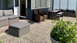 An outdoor patio with wicker furniture, a covered seating area, and a potted plant. - Bungalow Near Beach With Garden (Sint Maartensvlotbrug)