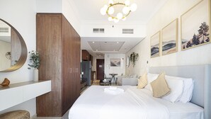 A modern bedroom with a large bed, a wooden wardrobe, a vanity with a mirror, and a dining area in the background. - Lake View Studio near Marina with Pool, Balcony and Gym (Dubai)