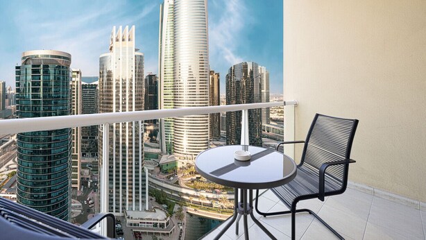 A balcony with a table and chairs, overlooking a cityscape with modern high-rise buildings. - Lake View Studio near Marina with Pool, Balcony and Gym (Dubai)