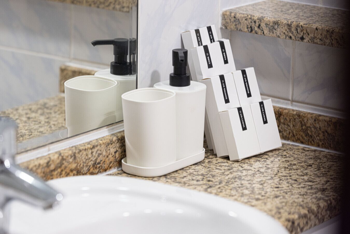 A bathroom with a granite countertop, a white sink, and two white dispensers with black pumps.