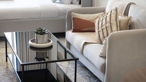 A modern living room with a glass coffee table, a sofa with decorative pillows, and a small potted plant. - Lake View Studio near Marina with Pool, Sauna and Gym (Dubai)