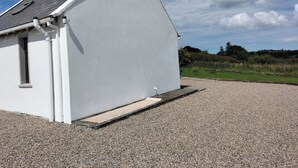 A white building with a sloped roof, a small window, and a gravel driveway. - Creeslough - 2 Bed Cottage - Pet Friendly - Garden (Glenveagh)