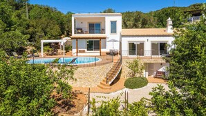 Une maison moderne à deux étages, dotée d’une piscine, d’un patio couvert et d’un escalier en pierre menant à l’étage supérieur.