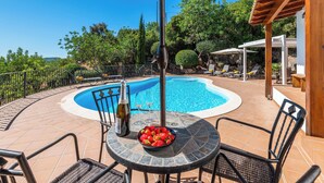 Un espace piscine doté d’une piscine circulaire, de chaises longues, d’une table sur laquelle se trouve un saladier rempli de fraises et d’une pergola.