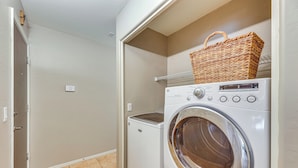 A laundry room with a front-loading washing machine and dryer, a wicker basket on the dryer, and a tiled floor. - 5 Mi to Downtown - Peaceful Home in Casa Grande (Casa Grande)